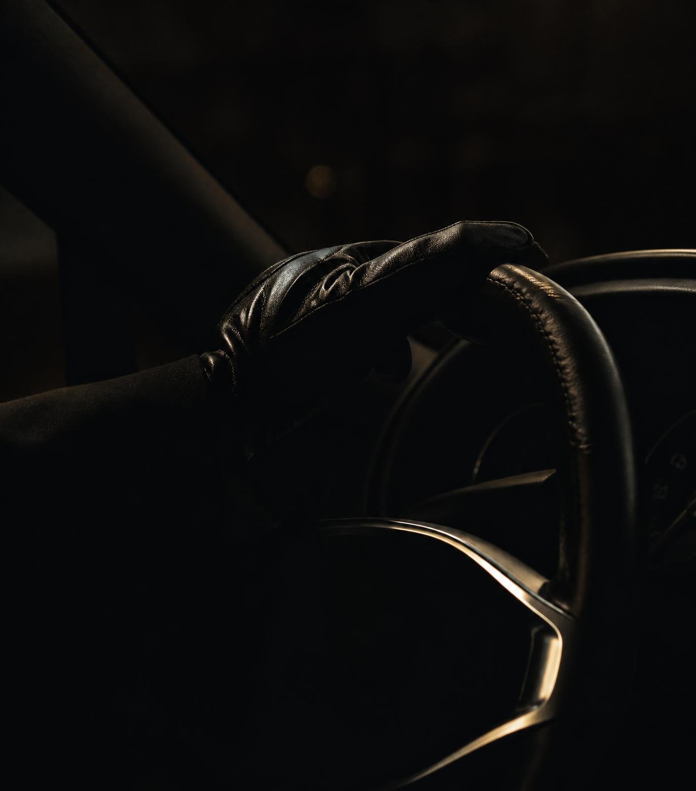 Gloved hand resting on the leather steering wheel of a luxury car at night